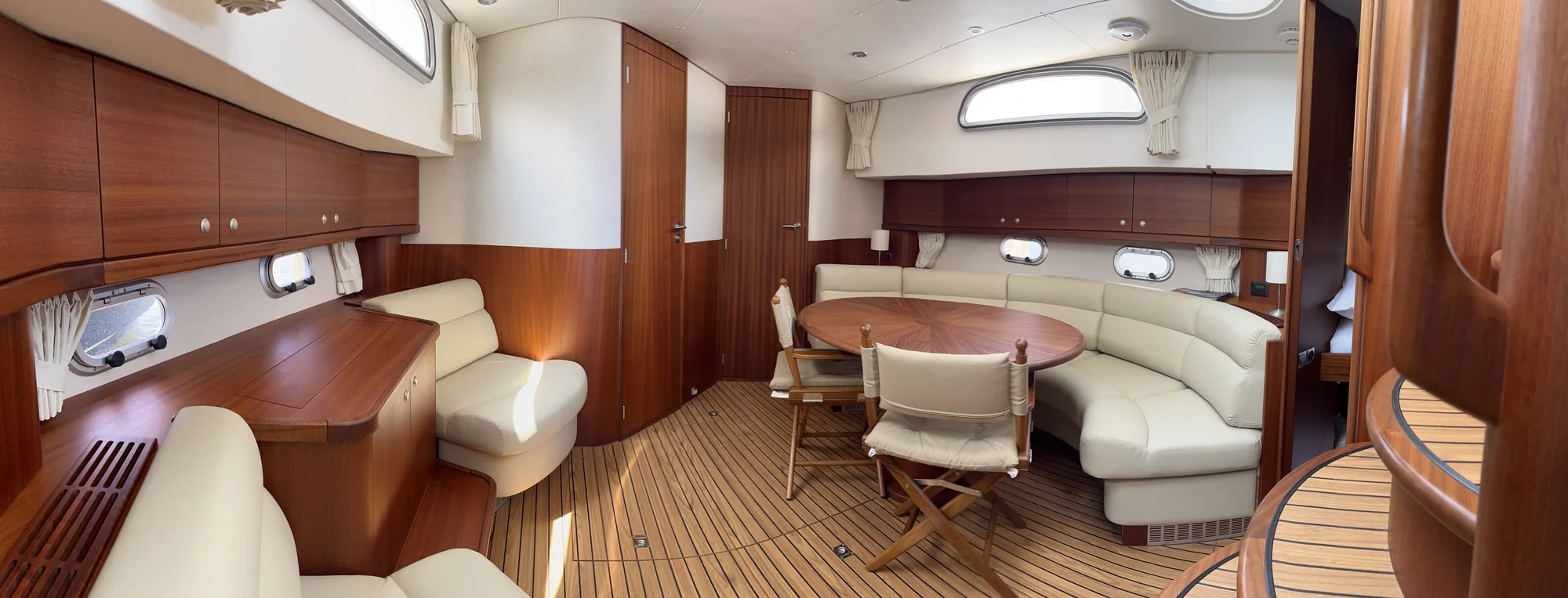 Wide salon aboard E4-301, with Satin Mahogany cabinetry, cream seating and an oval dining table.