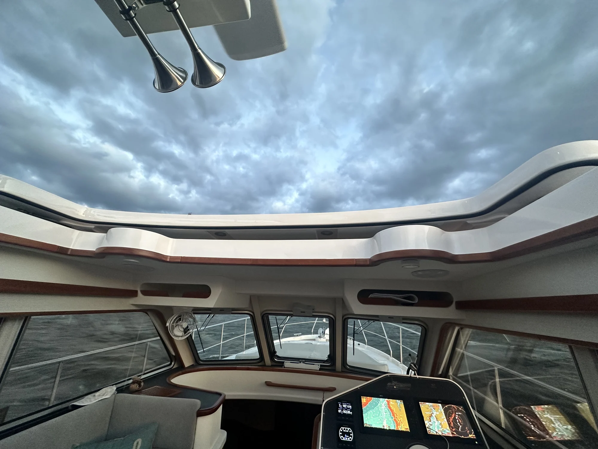 View from the E4-337 wheelhouse through its open roof, with the helm, forward windows and cloudy sky visible.