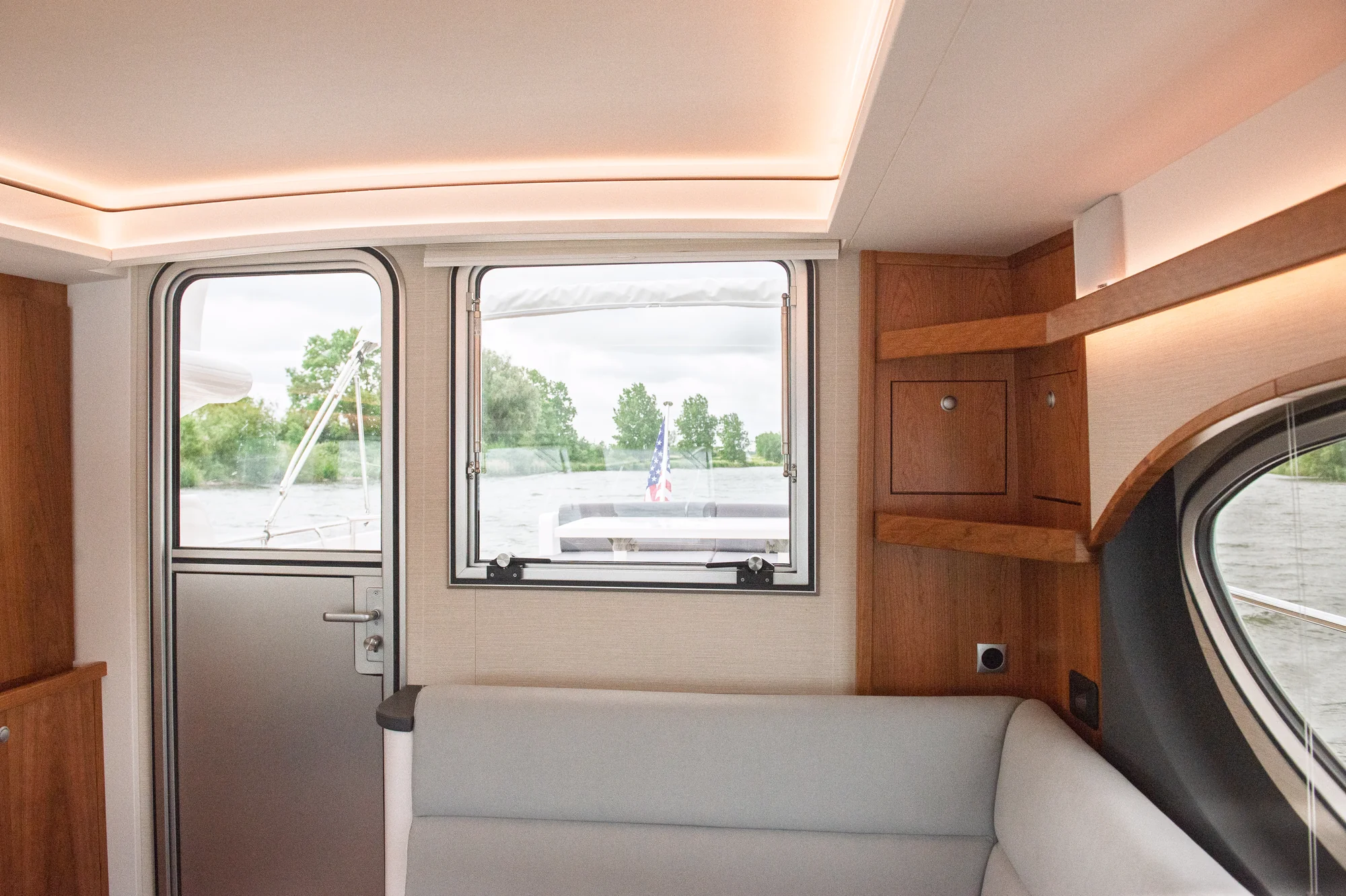 E4-343 wheelhouse seating with light upholstery, Satin Cherry cabinetry, an oval side window and the aft door.