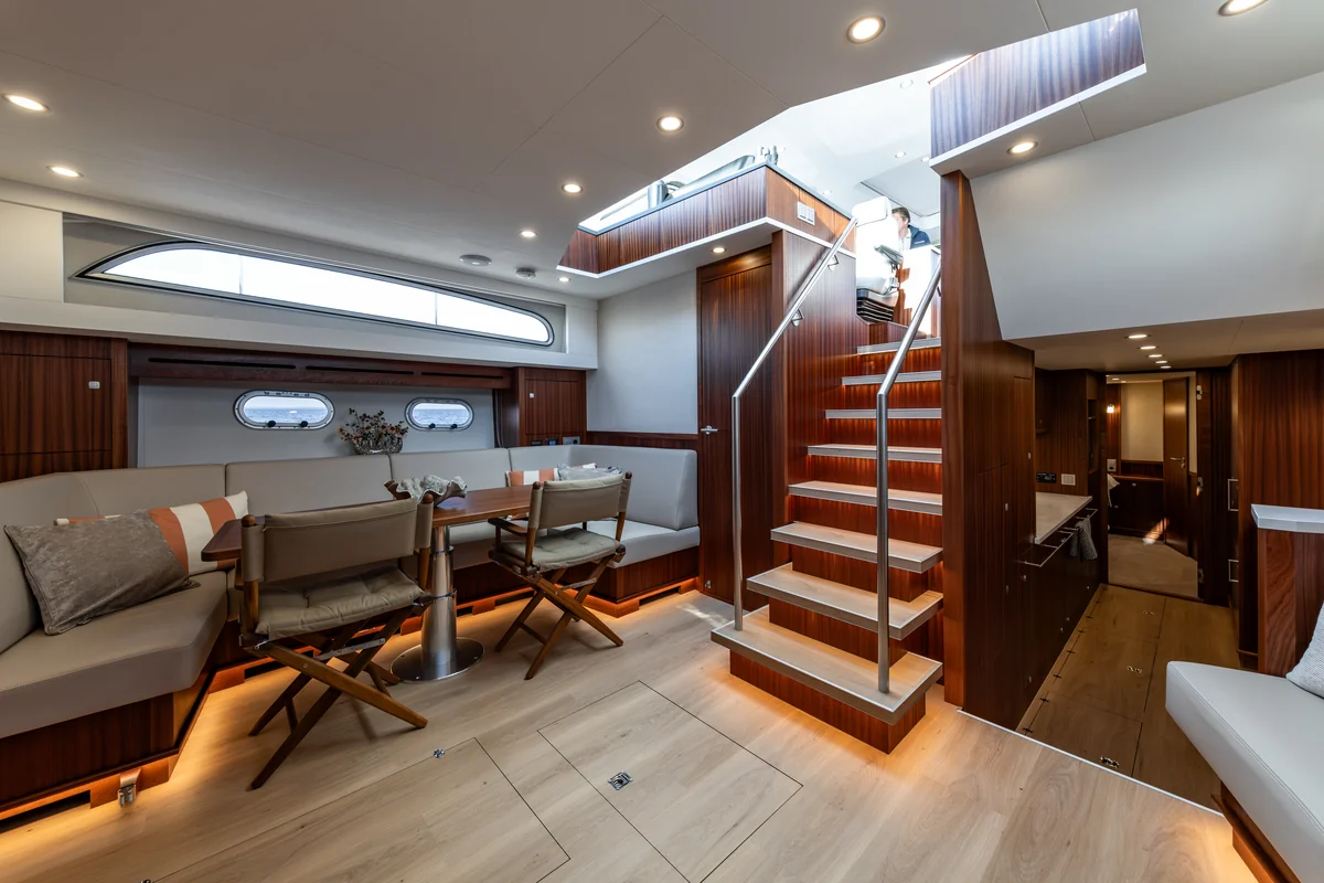 Elling E6 lower salon with a long upholstered sofa, wood table, two chairs and an illuminated staircase.