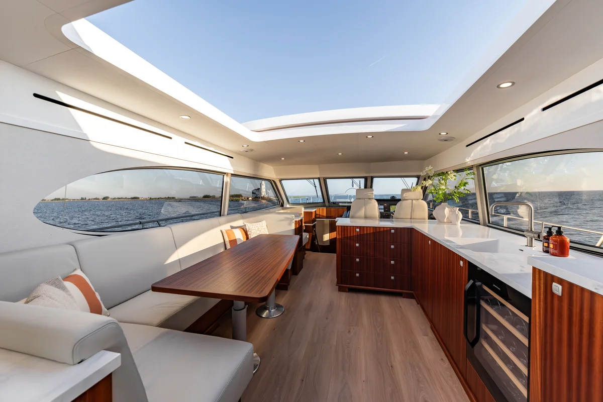 Elling E6 upper salon with cream seating, a wood table, panoramic windows and an open roof.